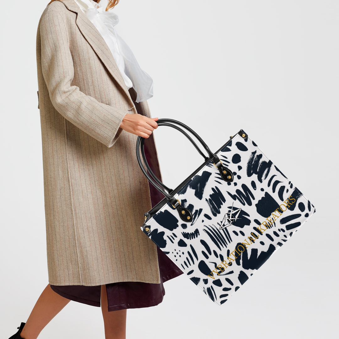 Kreator Luxe tote bag by Vybrational Kreators featuring a black and white abstract pattern structured shape black top handles gold hardware and printed brand logo.